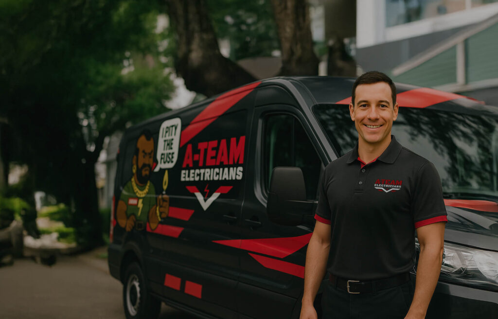 A-Team Electricians van parked with a logo and catchy slogan, featuring a person in a branded polo shirt standing beside it.